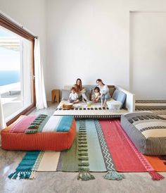 three people sitting on a couch in a living room with colorful rugs and pillows