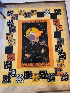 an orange and black quilt on the floor with bats, pumpkins, and stars