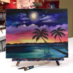 an easel with a painting on it that has palm trees and the sun in the sky