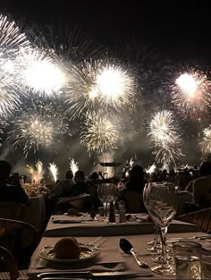 fireworks are lit up in the night sky over a table with plates and wine glasses