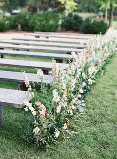 rows of wooden benches lined up in the grass with flowers growing out of each row