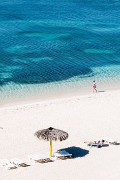 people are walking on the beach with umbrellas and lounge chairs in front of them