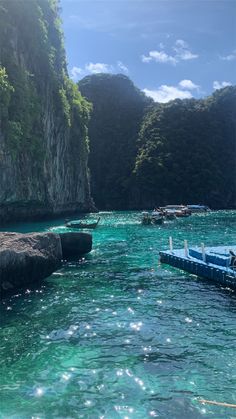 several boats floating in the water next to some rocks and cliffs with green trees on them