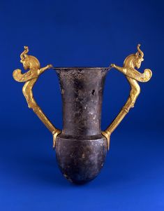 an antique vase with two handles and gold decoration on the top, against a blue background