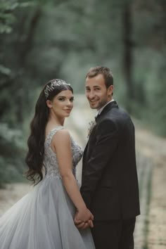 a man and woman standing next to each other in front of some trees wearing formal wear