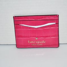 a pink card case sitting on top of a white counter next to a wall with a sign that says kate spade new york