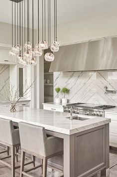 a kitchen with marble counter tops and an island in front of the sink is surrounded by hanging lights