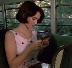 a woman sitting on a bus looking at her cell phone while holding something in her hand