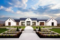 a large white house sitting in the middle of a lush green field next to mountains