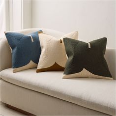 three pillows sitting on top of a white couch