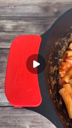 a pan filled with pasta and sauce on top of a wooden table next to a red spatula