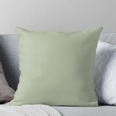 a light green pillow sitting on top of a gray couch next to pillows and blankets