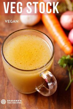 a glass mug filled with liquid sitting on top of a wooden table next to carrots