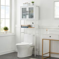 a white toilet sitting in a bathroom next to a sink and cabinet with glass doors