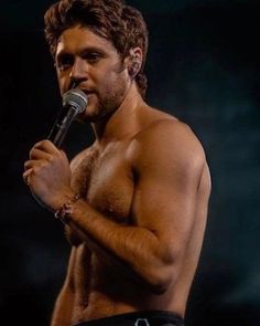 a shirtless man holding a microphone in his right hand