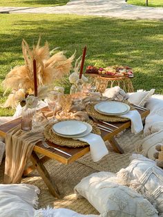 an outdoor table set with plates and napkins on it, next to some pillows