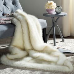 a white fur blanket sitting on top of a chair next to a table with a clock