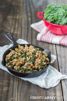 a skillet filled with meat and vegetables on top of a wooden table next to a red dish