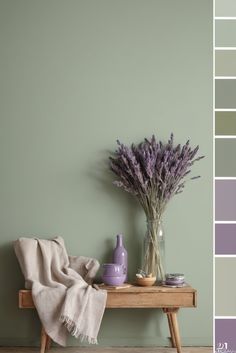 a wooden table topped with a vase filled with purple flowers next to a green wall