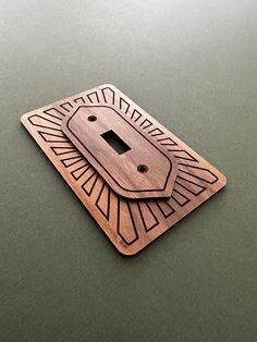 a wooden light switch cover on top of a green surface with an intricate design in the middle