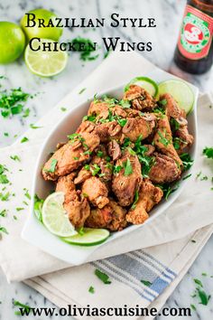 a white bowl filled with chicken wings and garnished with cilantro next to a bottle of booze