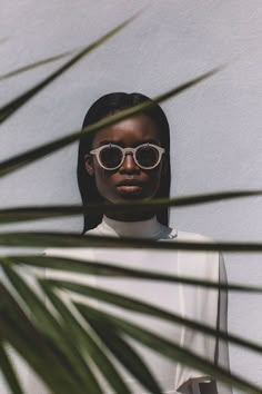 a woman wearing sunglasses standing in front of a plant