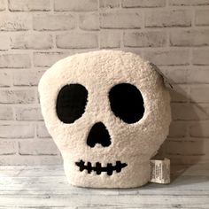 a white and black skull shaped pillow sitting on top of a wooden table next to a brick wall