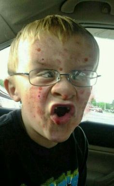 a young boy wearing glasses and sticking his tongue out in the back seat of a car