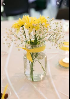 yellow flowers are in a mason jar on a white tablecloth with candles and other decorations