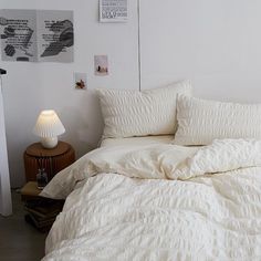 an unmade bed with white comforter and pillows in a small room next to a night stand