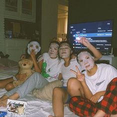 group of kids with face masks on sitting on bed in front of tv and holding up peace sign