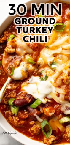 a white bowl filled with turkey chili and topped with sour cream, green onions and cheese