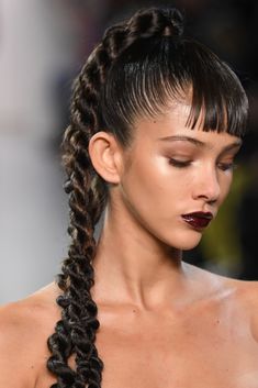 a woman with long braids on her head and red lipstick in her mouth, looking down at the camera