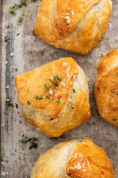 four baked pastries sitting on top of a baking pan covered in cheese and herbs