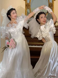 two women in white dresses standing next to a piano