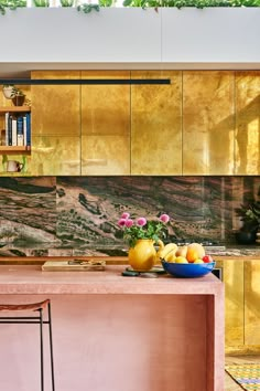 a bowl of fruit is on the kitchen counter next to a vase with flowers in it