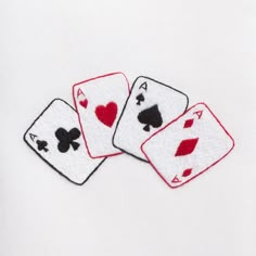 three playing cards with hearts and spades embroidered on the front, sitting on a white surface