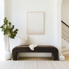 a white living room with a black bench and some vases on the floor next to it