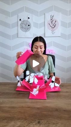 a woman sitting at a table with pink paper flowers in front of her face and hands