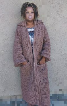 a woman standing in front of a wall wearing a long crochet cardigan