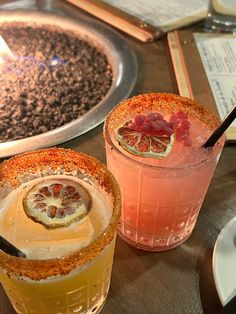 two cocktails sitting on top of a table next to each other with drinks in front of them