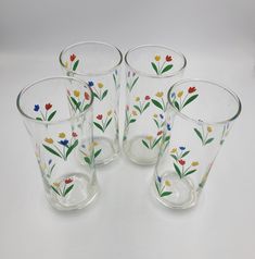 four glass cups with flowers painted on them are sitting next to each other and one is empty