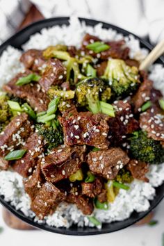 beef and broccoli stir fry with rice in a black bowl on a white surface