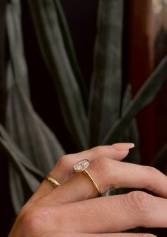 a woman's hand with a ring on it and a plant in the background