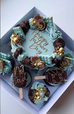 a birthday cake decorated with chocolates and gold decorations in a blue box on top of a table