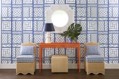 two chairs and a table with a mirror on it in front of a blue patterned wall