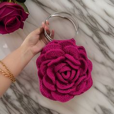 a pink crocheted rose purse being held by a woman's hand on a marble surface