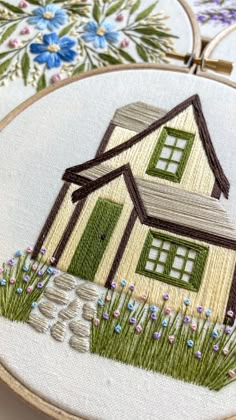 a small house is embroidered onto a white fabric with green trim and flowers on it