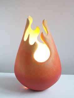 an orange vase with flames on it sitting on a white table top next to a wall