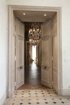 an open door with chandelier hanging from it's sides in a hallway